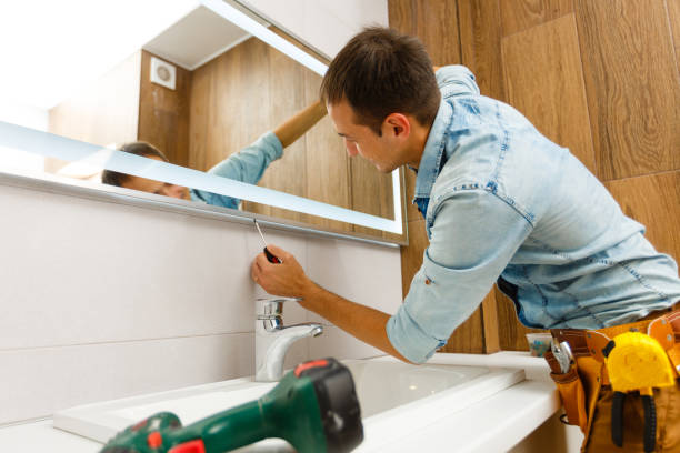 Man installing a mirror on wall in his renewed bathroom by Bathrooms by RUPP
